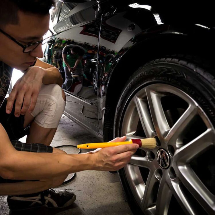 Osoba koristi žutu četku od prirodnih vlakana za čišćenje felne automobila.